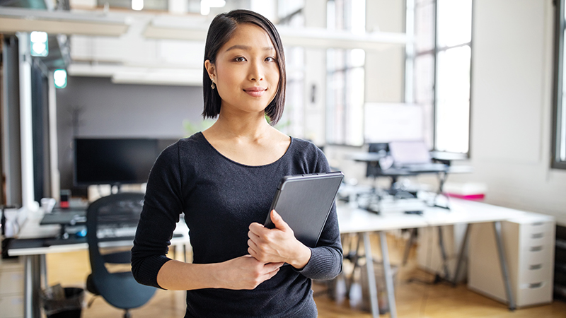 An Asian American women stands in an office and is holding a folder