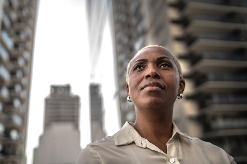 A business woman looks up and ahead of her with skyscrapers behind her