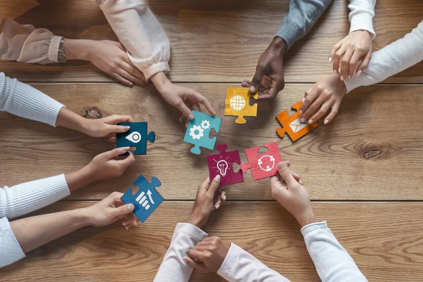 This stock image shows the hands of several people holding colorful puzzle pieces that fit each other. 